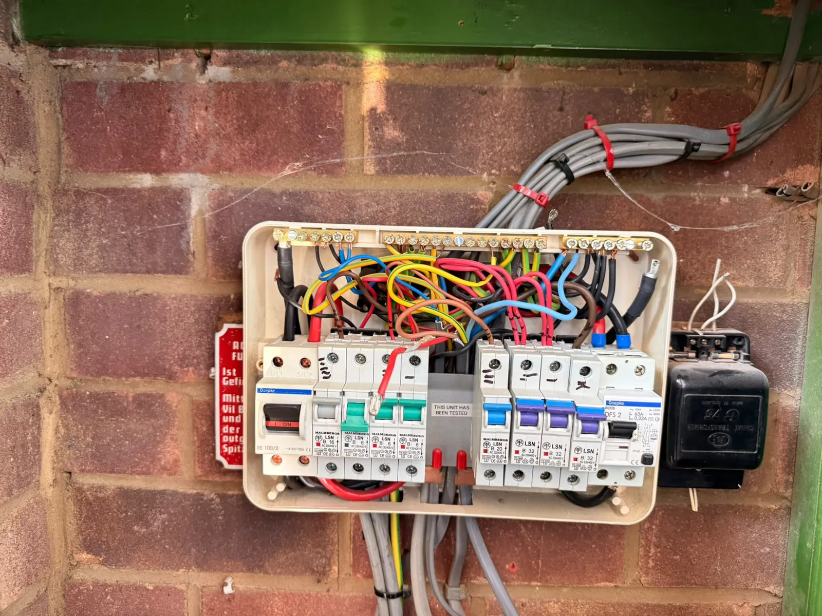 Old fuse board on a brick wall before a consumer unit upgrade