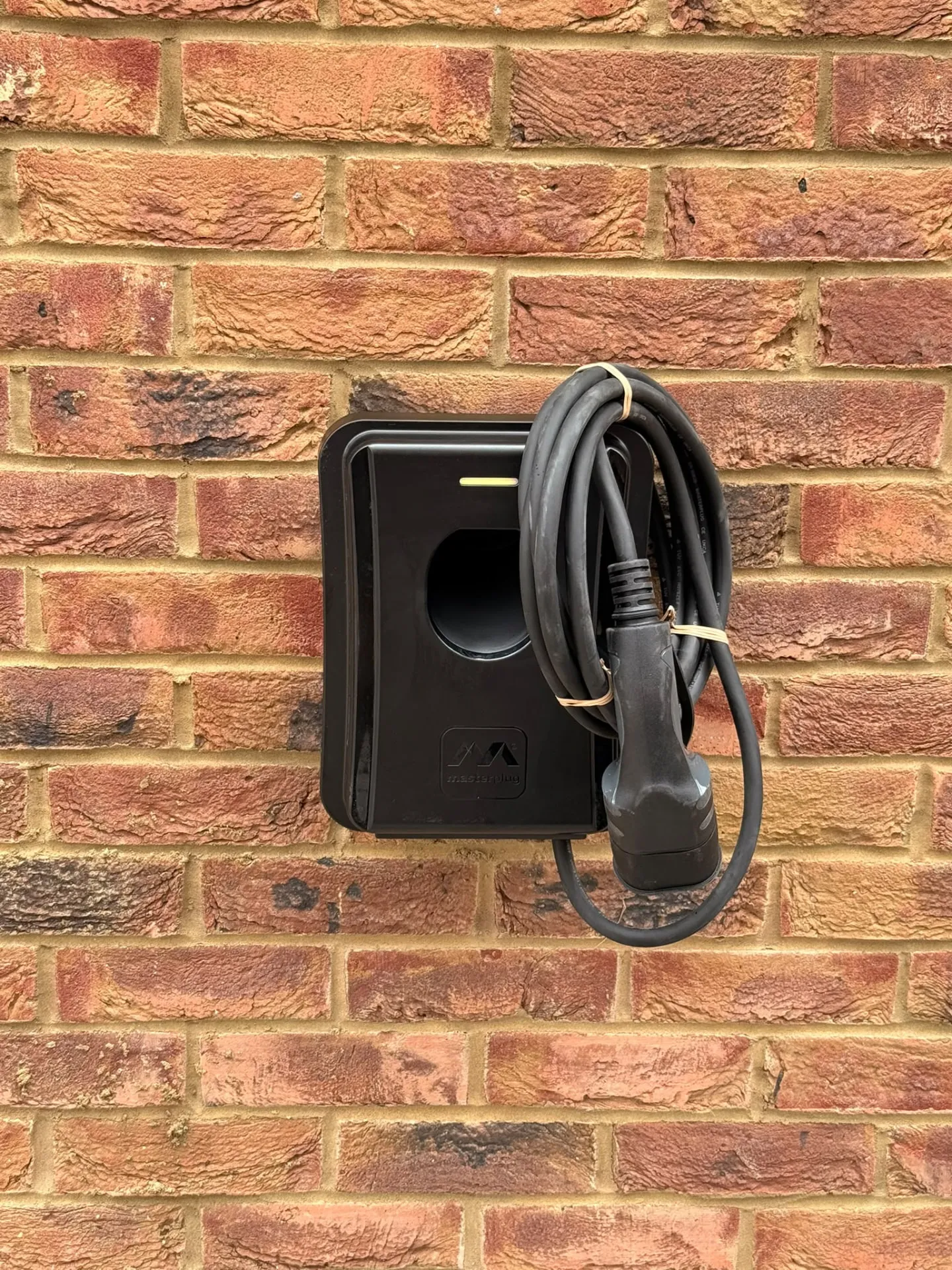 Black tethered home EV charger installed on a brick wall